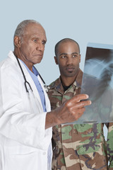 Wall Mural - Senior doctor with US Marine Corps soldier looking at x-ray report over light blue background