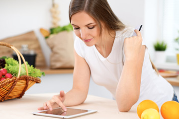 Young woman is making online shopping by tablet computer and credit card. Housewife found new recipe for  cooking in a kitchen