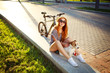 Smiling Hipster Girl with her Dog and Bike Relaxing in Park. Happy Woman Enjoying Summer Lifestyle with Pet. Candid Toned Photo with Copy Space.