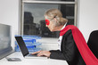 Side view of senior businesswoman in superhero costume using laptop at office desk