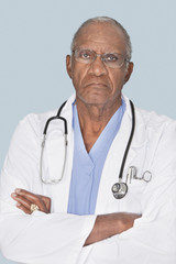 Wall Mural - Portrait of a senior doctor with arms crossed over light blue background
