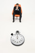 Anxious businessman sitting on chair with stopwatch in front of him representing loss of time
