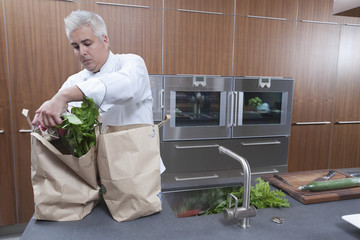 Wall Mural - Male chef unpacking groceries from paper bags in commercial kitchen