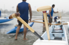 Wooden Oars On Outrigger Canoe With Canoeists In Background At Beach