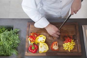 Wall Mural - Midsection of male chef dicing red and yellow bell peppers in commercial kitchen