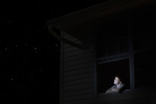 Young Boy At Open Window Looking At Night Sky