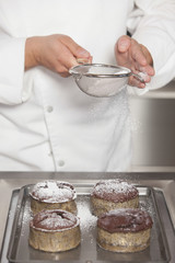 Wall Mural - Midsection closeup of male chef icing sugar over chocolate cakes at counter in commercial kitchen