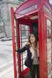 Happy young woman opening door of telephone booth at London, England, UK