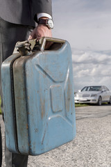 Wall Mural - Low section of young businessman carrying gasoline can with broken car in background at countryside