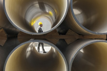Full Length Side View Of Young Male Architect Walking By Stacked Pipes At Construction Site
