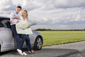 Wall Mural - Full length of couple with map discussing direction while leaning on car at countryside