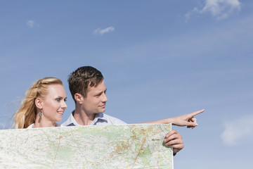 Wall Mural - Young man holding map while woman pointing away against sky