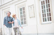 © MDBPIXS - Happy middle-aged tourist couple walking arm in arm by building