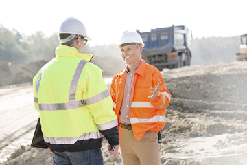 Happy engineer talking to colleague at construction site on sunny day