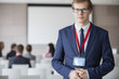 © MDBPIXS - Portrait of confident businessman standing at seminar hall with colleagues sitting in background
