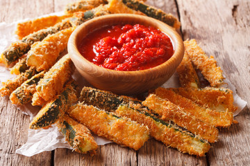 Fried slices of zucchini with parmesan cheese and breading and tomato sauce closeup on a table. horizontal