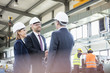© MDBPIXS - Businessmen shaking hands with workers working in background at metal industry