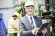 Portrait of confident mature businessman using digital tablet with worker in background at factory