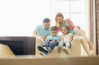 © MDBPIXS - Family looking at boy playing hand-held video game at home