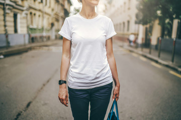 Front view. Cropped image. Summer day, a young woman in a white t-shirt standing on a city street. Wristwatch on the hand of the girl. Blurred background. Advertising space, mock up.