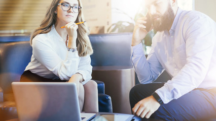 Wall Mural - Business meeting. Businessman and businesswoman are sitting in hotel lobby. Bearded man in talking on cell phone. On table are laptop and tablet computer. Teamwork, discussion of business plan.