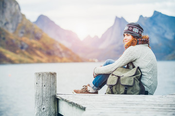 Woman traveler with a backpack sitting on a wooden pier.