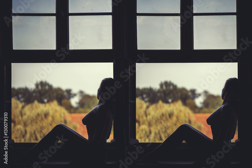 Fényképezés  Beautiful naked woman sitting on a window at sunset
