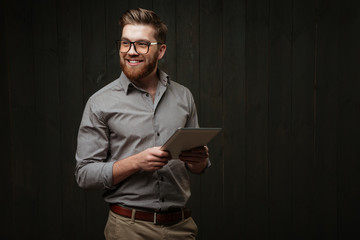 Wall Mural - Smiling man in eyeglasses holding tablet computer and looking away