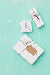 Wall Mural - Top view on nice Christmas gifts wrapped in white gift paper, Christmas tree decorations on turquoise wooden background with sparkling stars. New Year, holidays and celebration concept