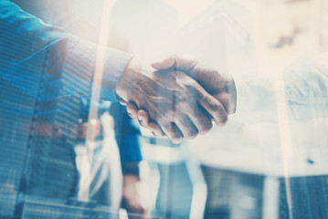 Double exposure concept.Close up view of business partnership handshake .Photo two businessman handshaking process.Skyscraper office building on the blurred background.Horizontal,flares effect.