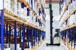 Warehouse worker on forklift pulls boxes from the top shelves in large, modern warehouse