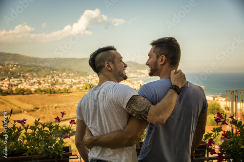 Back view of homosexual couple embracing nd looking at each other on background of resort Tablou Canvas