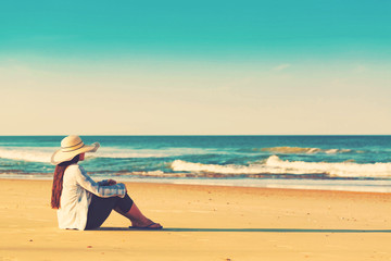 Wall Mural - Woman in a hat sitting on the beach