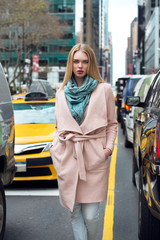 Wall Mural - Beautiful elegant blonde business woman walking out from the taxi on New York City street and walk throught the traffic wearing elegant pink jacket with scarf.