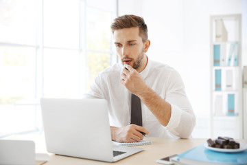 Sticker - Young man eating candies while working with laptop in office