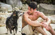 © theartofphoto - Young topless male in shorts sitting at beach and looking at dog near.