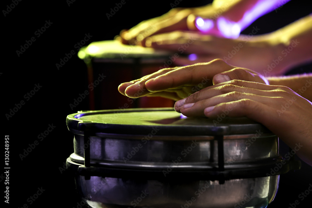 Hands of man playing African drum on dark background