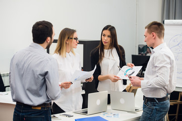 Four young business people working as a team gathered around laptop computer in an open plan modern office