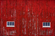Red barn wall with windows and aged red paint peeling off boards