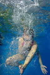  A little girl goes in for sports in the swimming pool and dives under the water in bubbles. Portrait. Shooting underwater. Vertical orientation