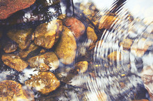 Concentric Ripples And Sky And Tree Reflections In A Shallow Pebble Filled Stream Bed. Retro Toned Image.