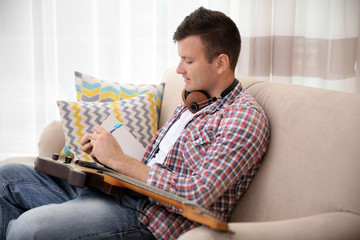 Wall Mural - Young man with headphones composing music and sitting on the couch