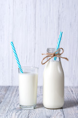 Bottle and glass of milk with blue straws, wooden background