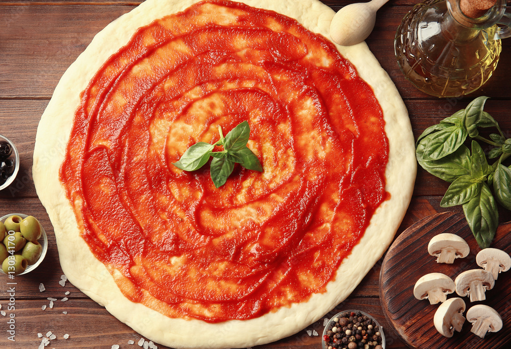 Raw pizza dough with sauce and ingredients on wooden table