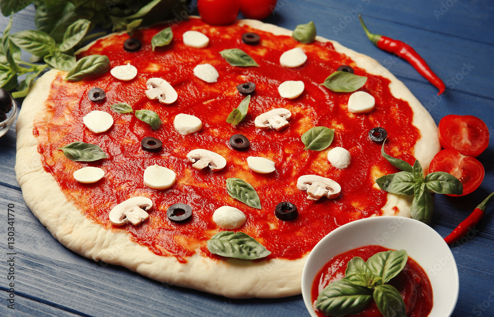 Raw pizza dough with sauce and ingredients on wooden table