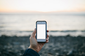 man's hand holding a phone on the background of beach. Copy space