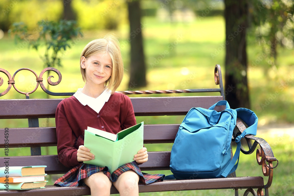 Schoolgirl reading book while sitting on bench in park