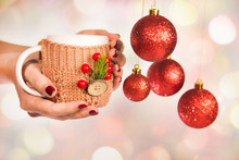 Close Up Of Winter Holiday Cup In Knitted Vintage Craft Cupholder With Christmas Decorations In Hands Of Woman With Beautiful Festive Red Manicure And New Year Hanging Balls. Horizontal Color Photo