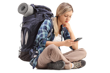 Wall Mural - Female hiker sitting on the ground and looking at a cell phone