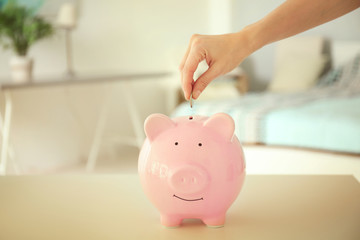 Sticker - Savings concept. Female hand putting coin into piggy bank on table